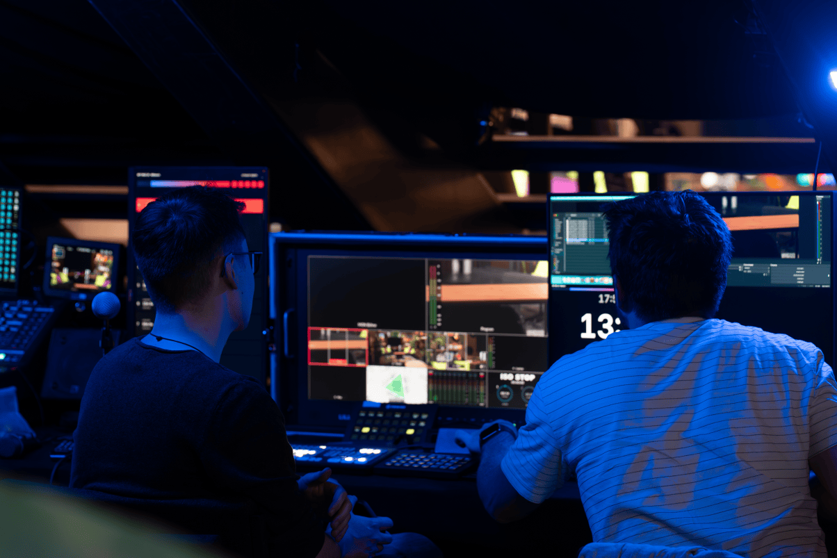 Menschen sitzen vor Monitoren einer Fernsehübertragung