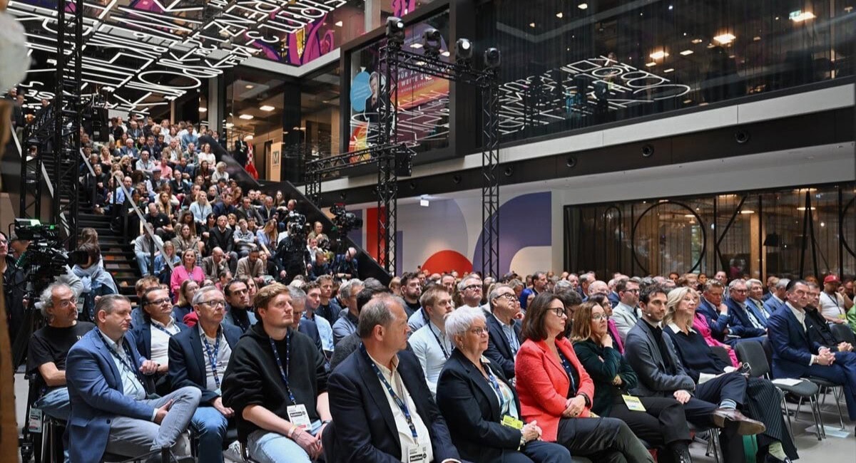 Eine voll gefüllte Halle mit zuhörenden Menschen auf einer Konferenz