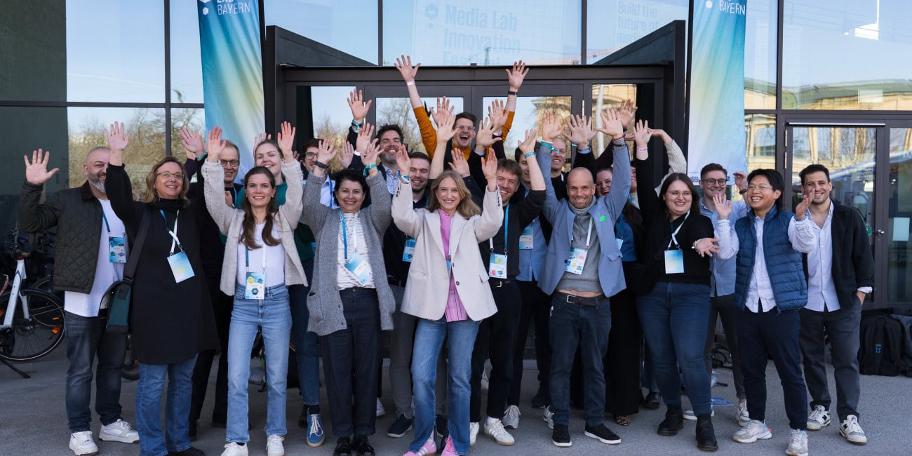 Die Teilnehmenden des Strategie Sparrings sind hier auf einem Gruppenfoto zu sehen. Alle strecken freudig lachen die Hände in die Luft.