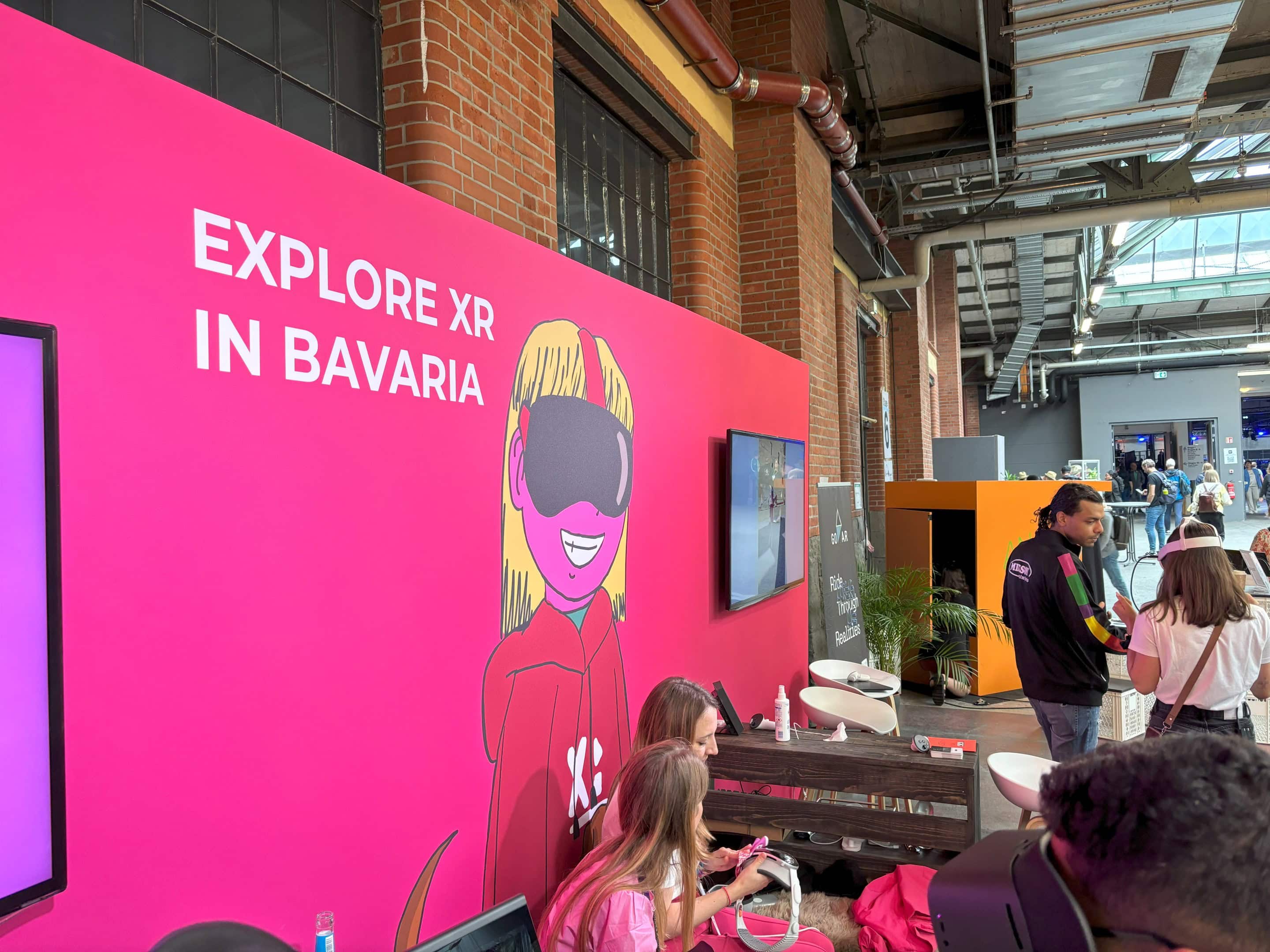 Eine Messestandwand im pink der Initiative XPLR: Media in Bavaria mit dem Schriftzug Exlplore XR in Bavaria